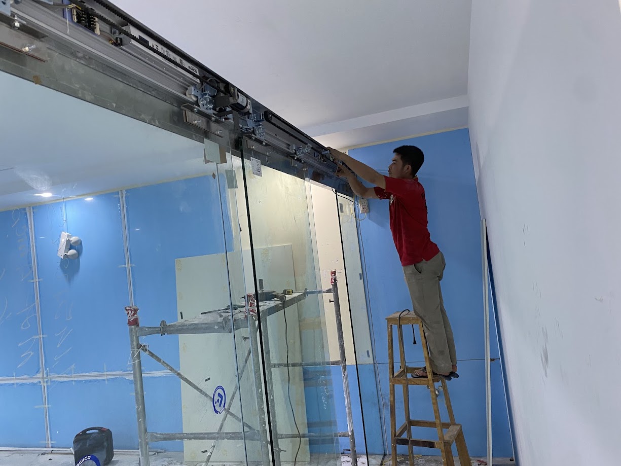 Kỹ thuật viên lắp đặt cửa kính trượt tự động khung nhôm trong nhà xưởng nội thất